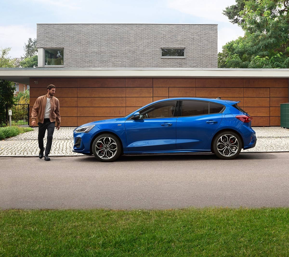 Ford Focus blu. Vista laterale, parcheggiata davanti a un edificio. Un uomo le passa a fianco.