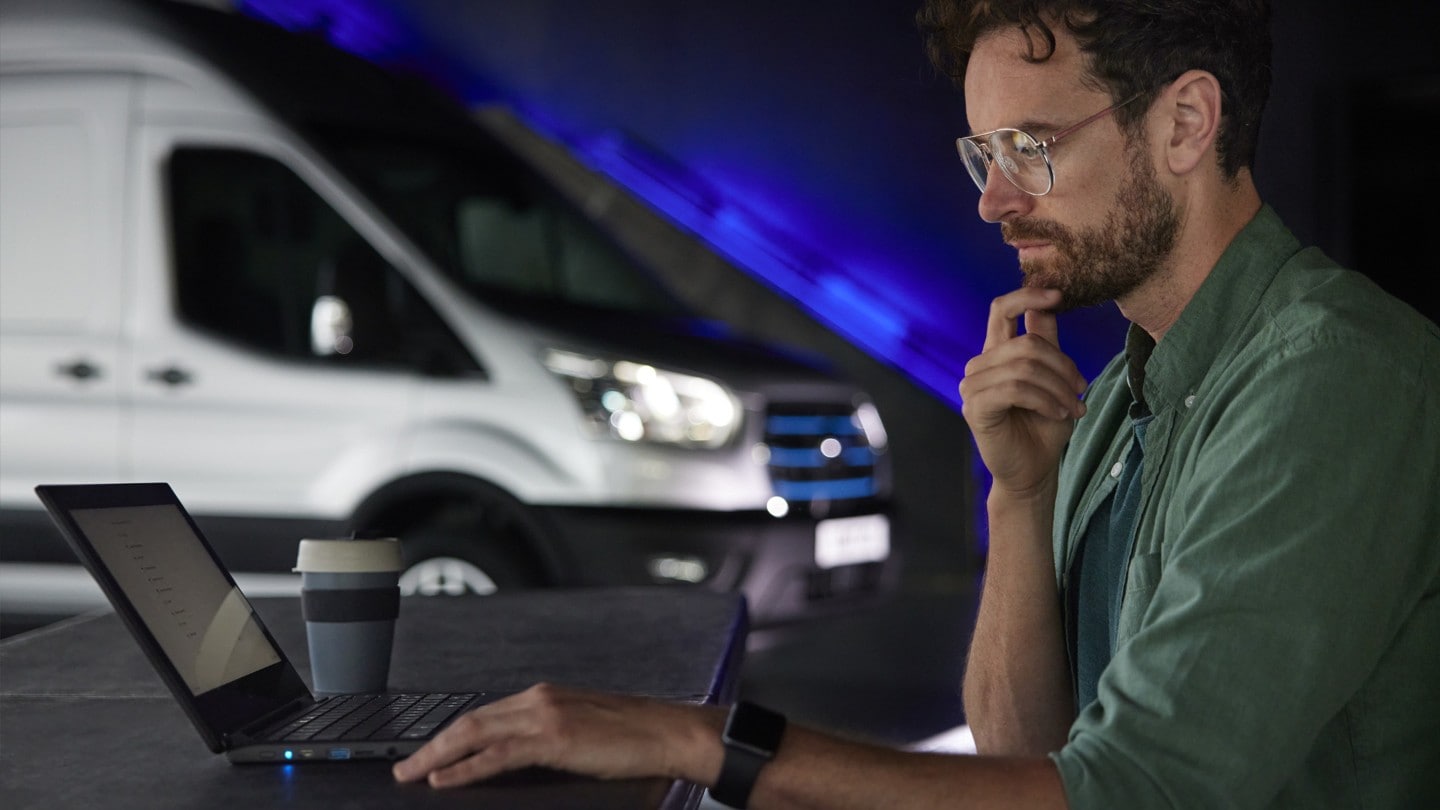 Un uomo è seduto davanti a un computer portatile, sullo sfondo si intravede un Ford E-Transit