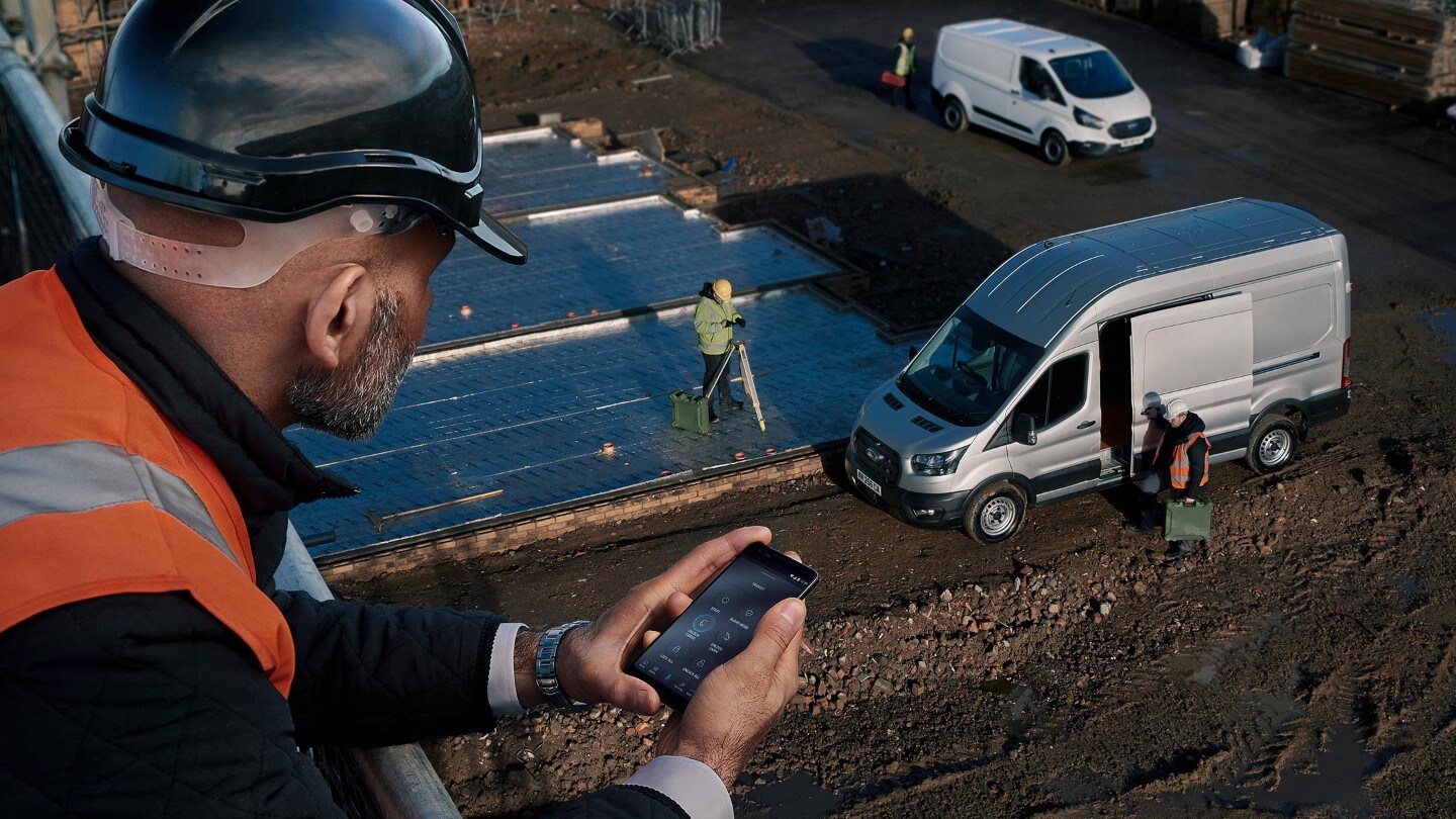 Un lavoratore con un caschetto blu guarda un veicolo aziendale da un edificio