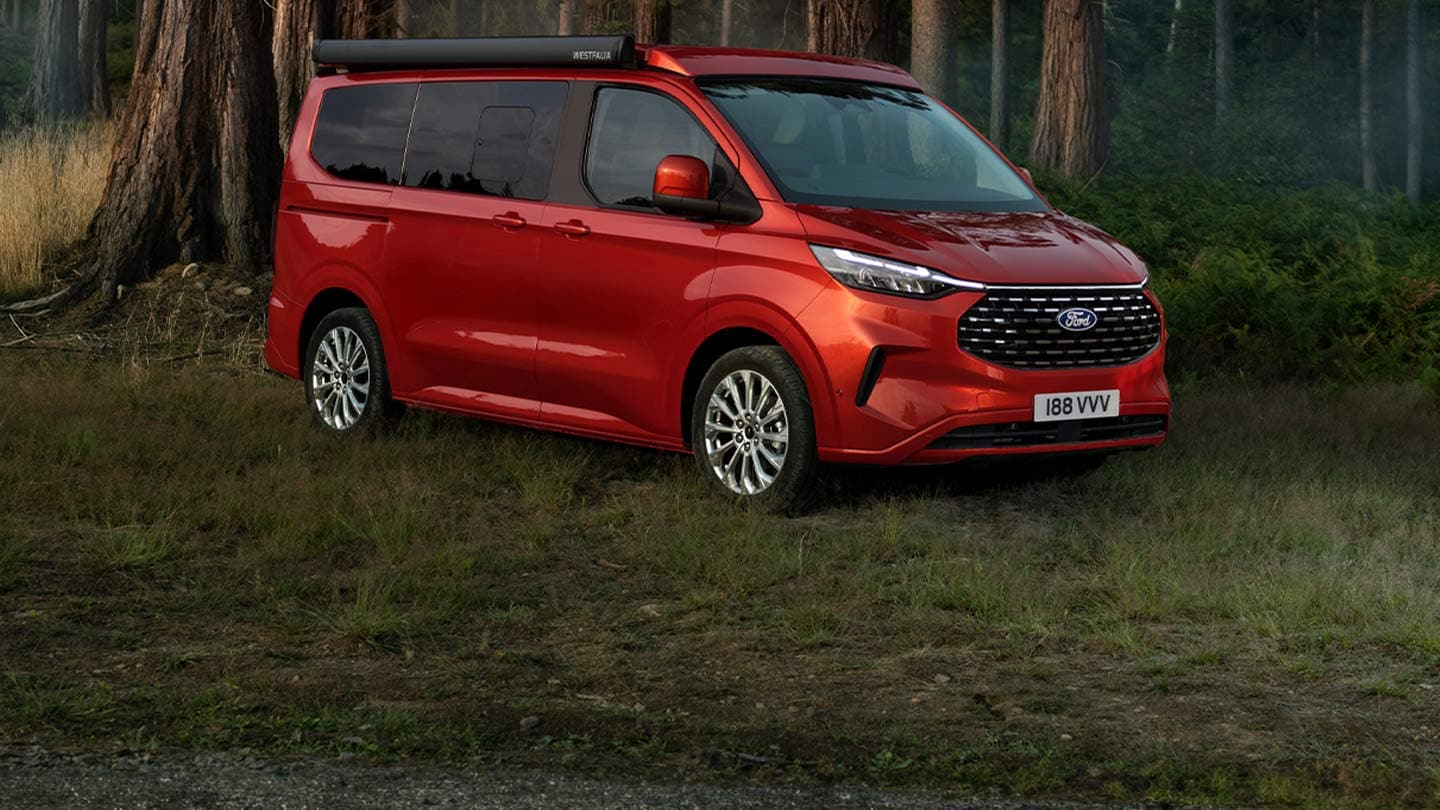 Ford Nugget rosso. parcheggiato su un prato nel bosco.