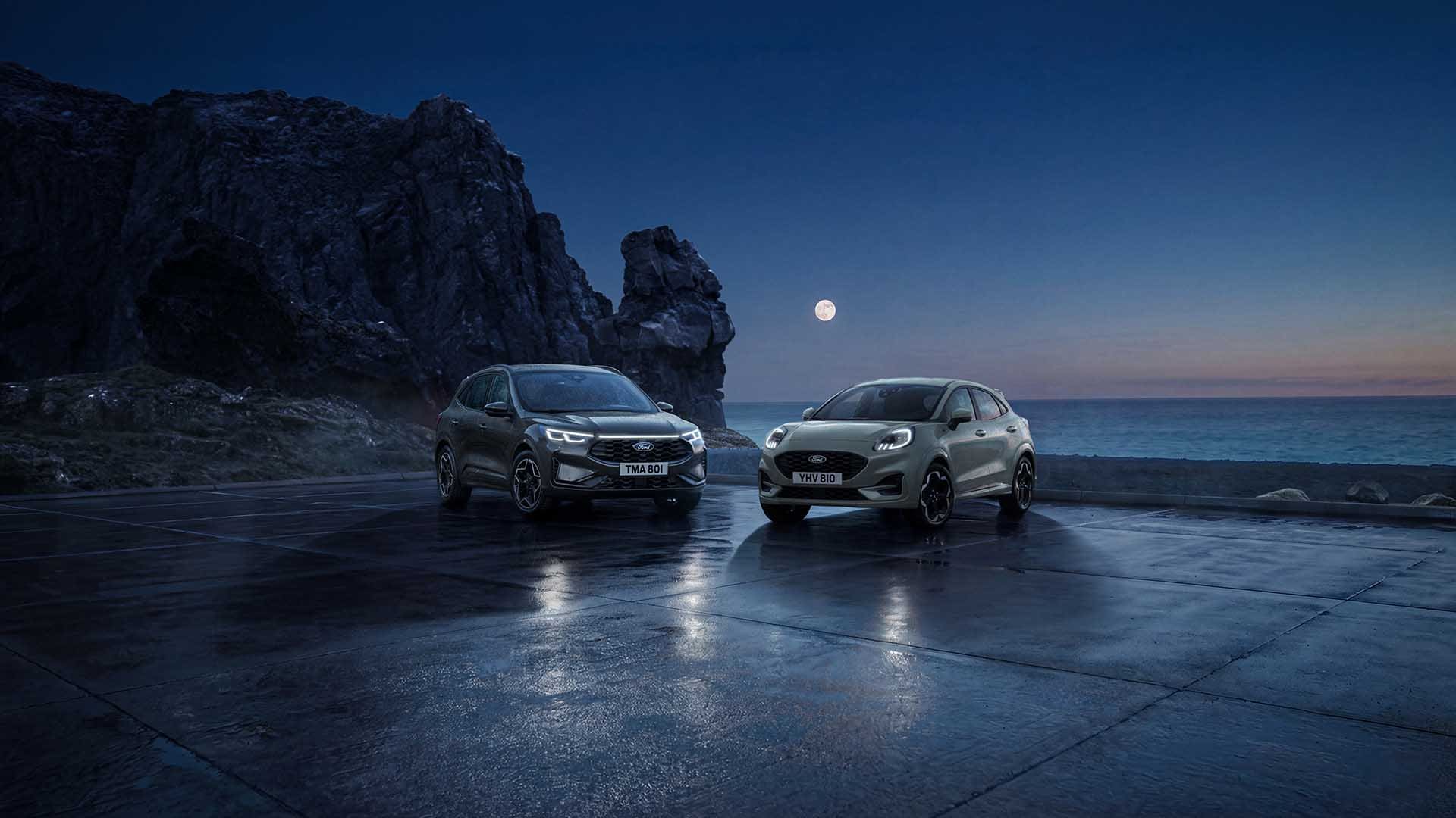Una Ford Kuga e una Ford Puma parcheggiate di notte sulla costa sotto la luna piena.