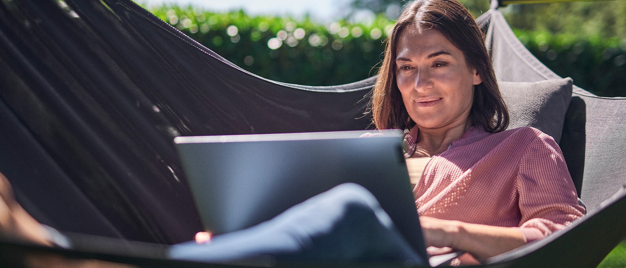 Persona rilassata su un'amaca che utilizza un laptop all'aperto.