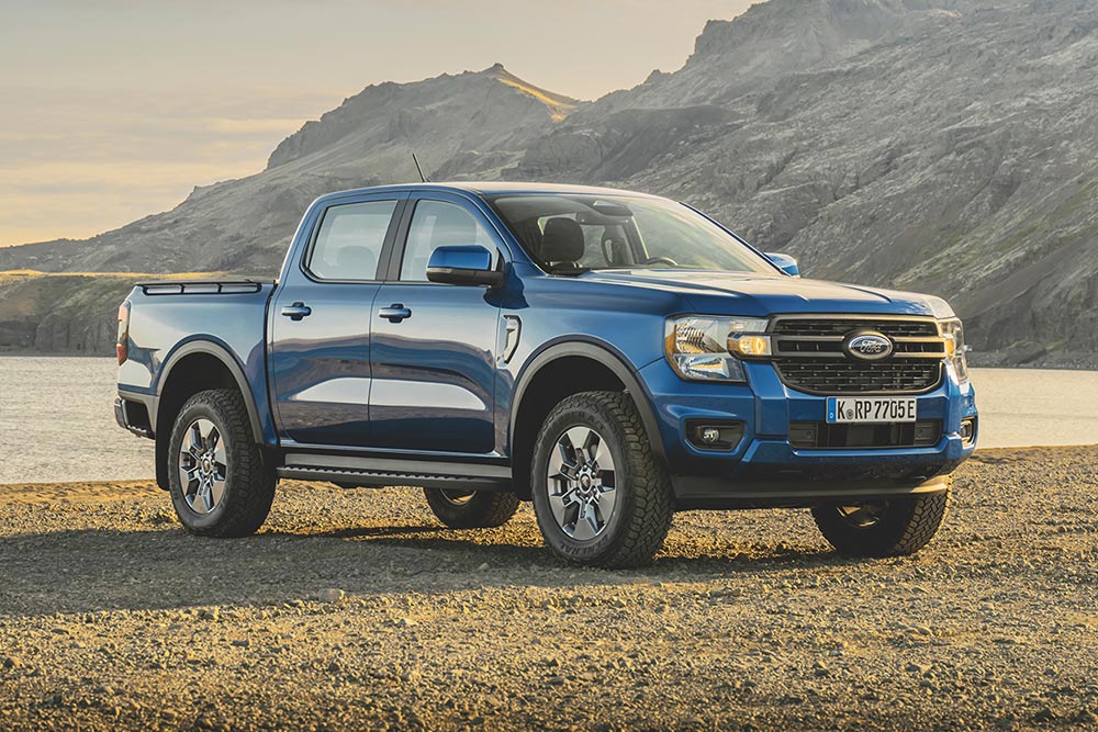 Un Ford Ranger blu sulle sponde di un lago, sullo sfondo montagne rocciose e scure nuvole dense.