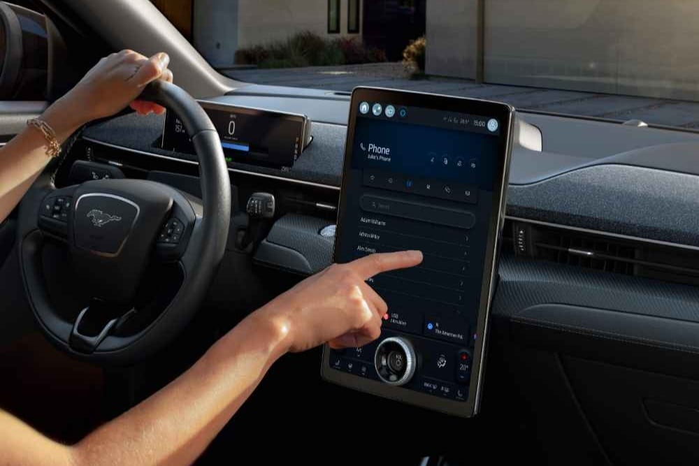 Primo piano del conducente di un Ford Mustang Mach-E che interagisce con il grande touchscreen SYNC 4 da 15,5"