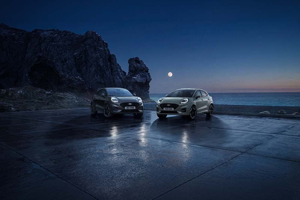 Due Ford Puma parcheggiate di notte sulla costa sotto la luna piena.
