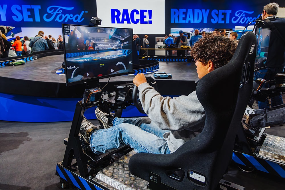 Un visitatore gioca a un simulatore di guida virtuale su un moderno stand Ford illuminato.