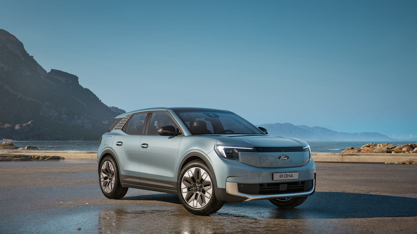 Vista laterale anteriore di una Ford Explorer argentata parcheggiata vicino a uno specchio d'acqua, con montagne sullo sfondo.