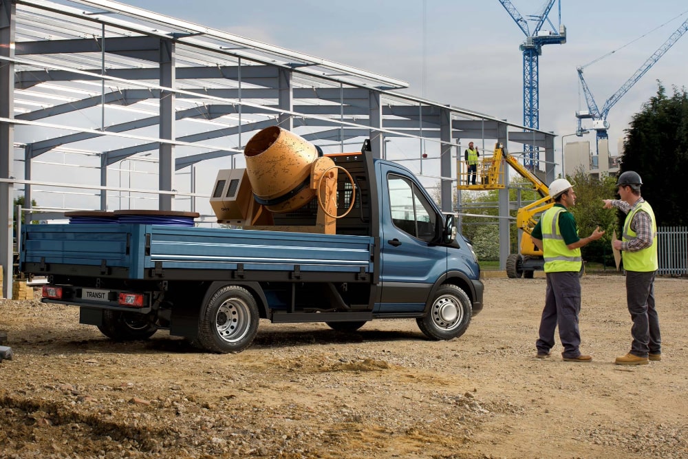 Vista laterale di un telaio cabinato Ford Transit blu, carico in un cantiere.