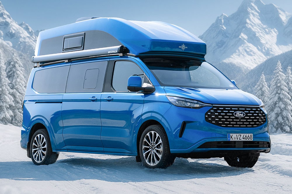 Vista anteriore a tre quarti di un Ford Nugget blu con tetto alto in sosta sulla neve davanti a un panorama montano.