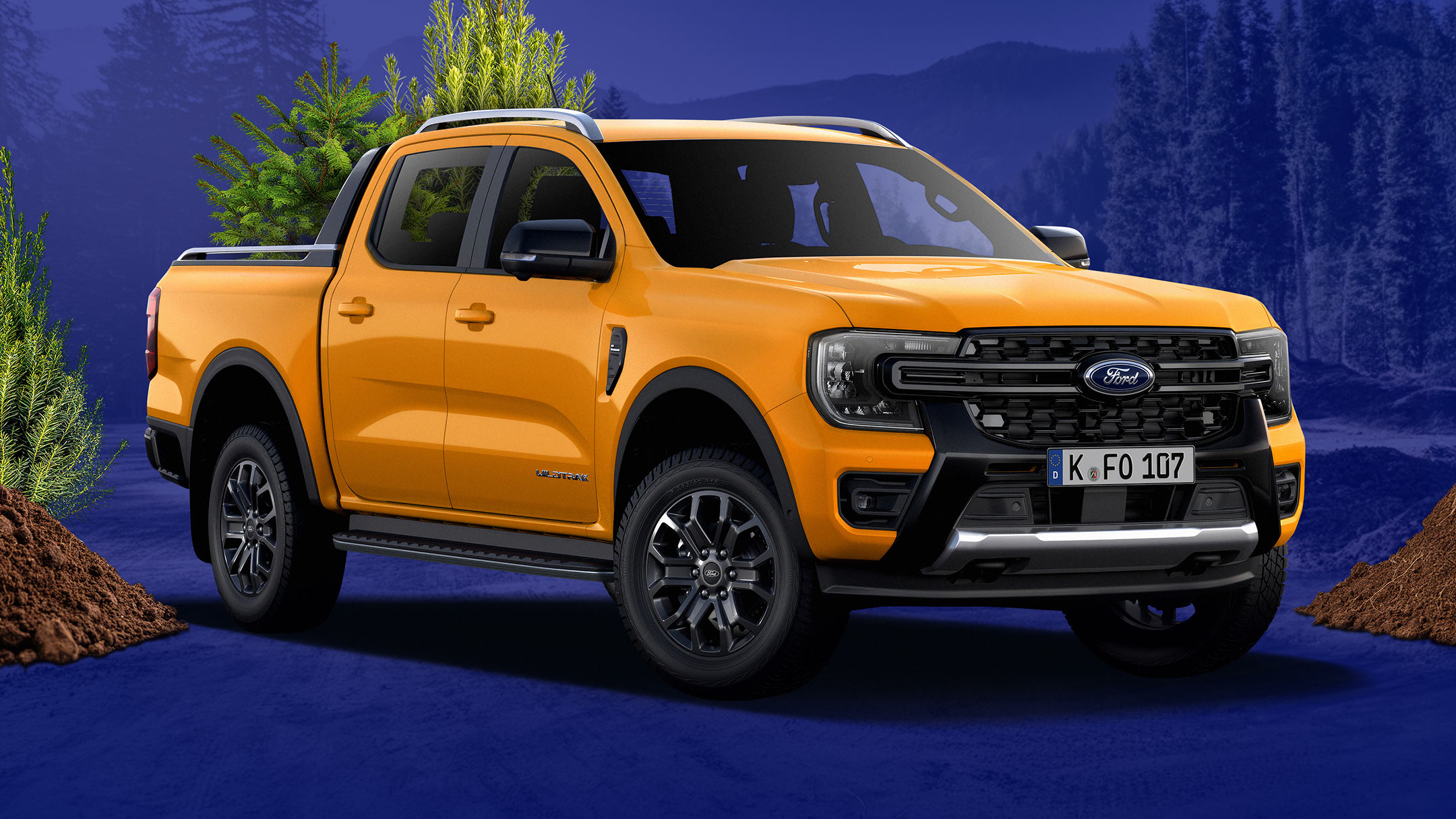 Ford Ranger giallo su sottofondo blu che trasporta alberi e terreno