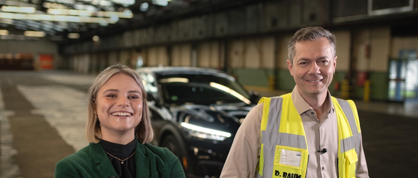 Una giovane donna e un collaboratore Ford sorridono verso l’obiettivo all’interno di un capannone