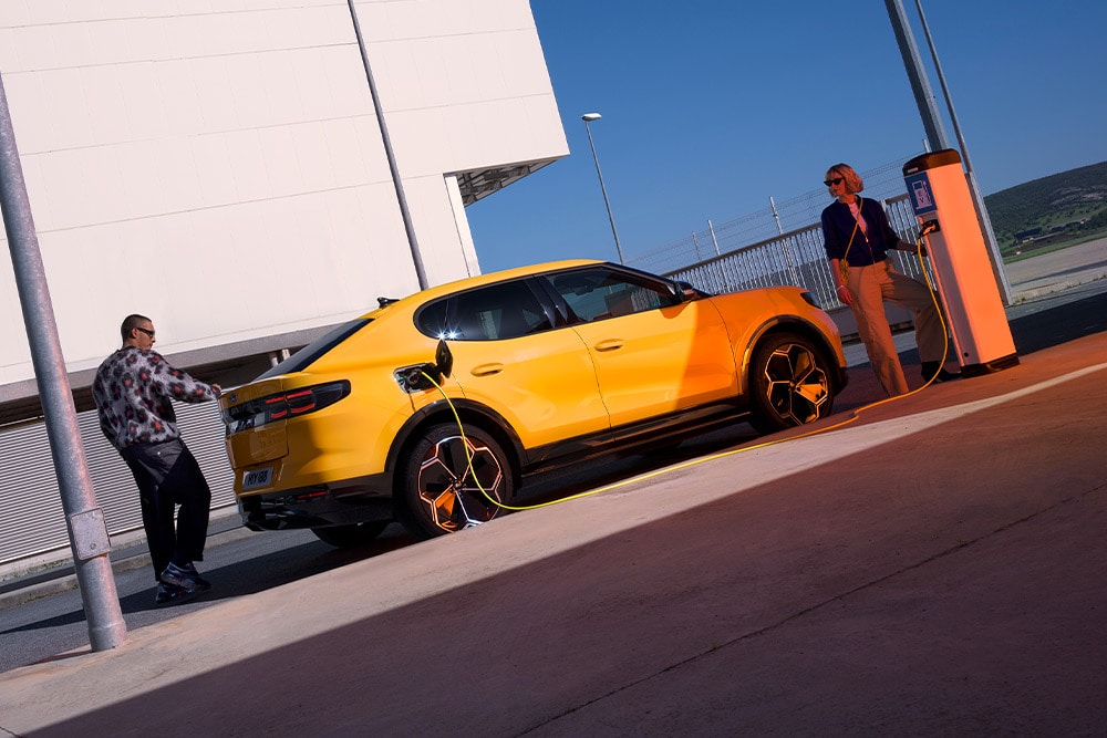 Delle persone ricaricano una Ford Capri elettrica gialla presso una stazione di ricarica pubblica.