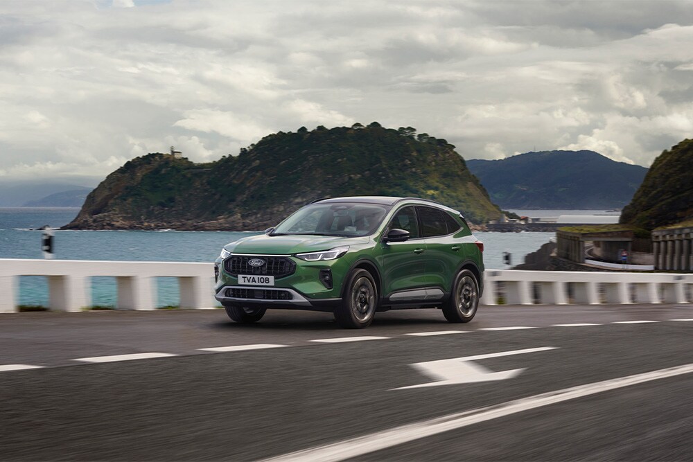 Una Ford Kuga Hybrid autoricaricante verde in marcia su una strada panoramica.
