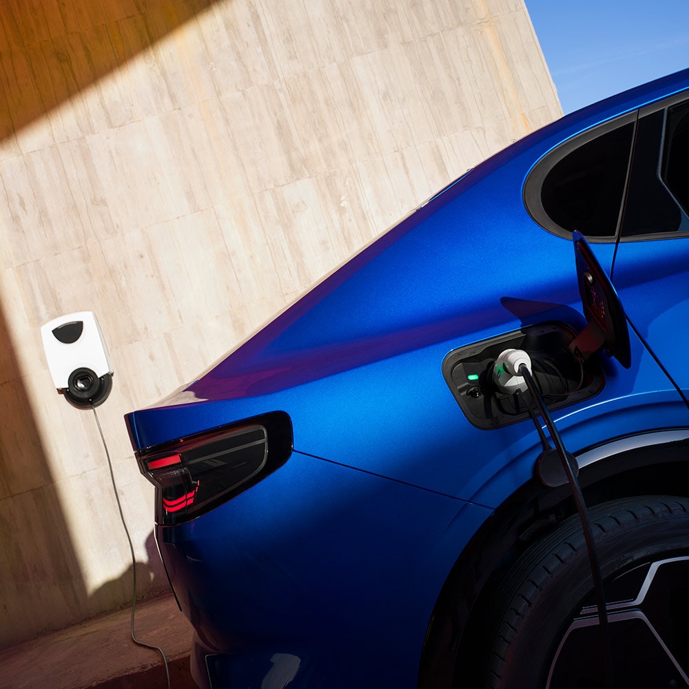 Vista posteriore di una Ford Capri elettrica blu che è collegata a una stazione di ricarica per veicoli elettrici.