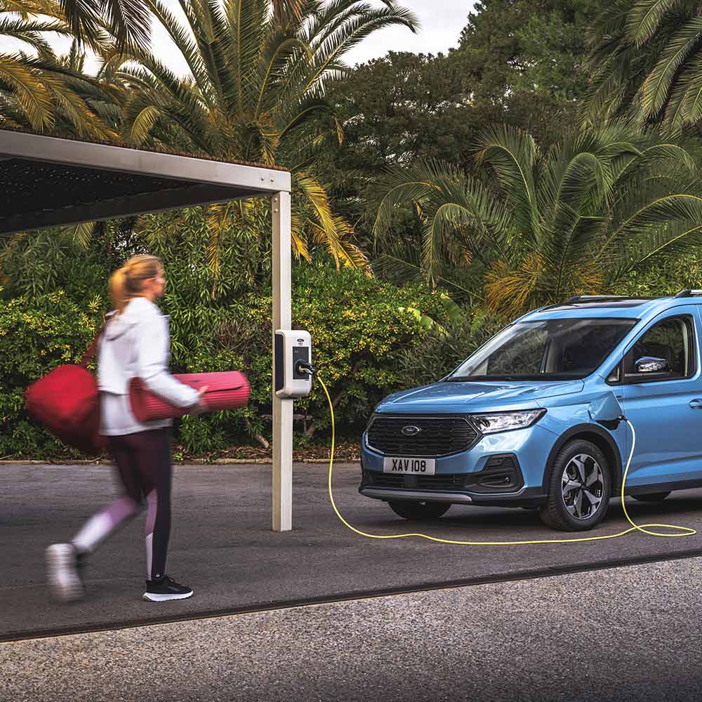 Una persona con un tappetino per lo yoga si avvicina a un Ford Tourneo Connect Plug-in-Hybrid.