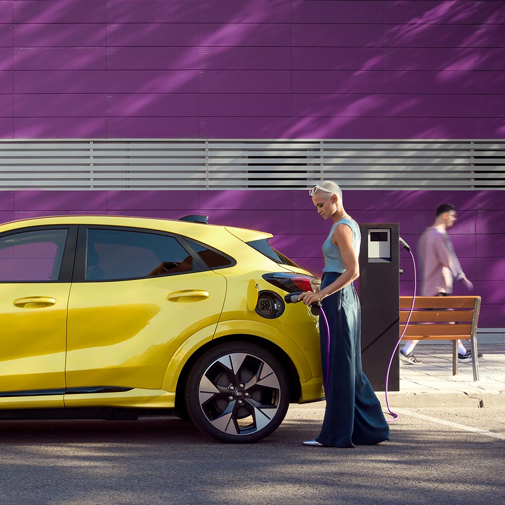 Un conducente collega una Ford Puma Gen-E gialla a una stazione di ricarica pubblica per un rifornimento elettrico agevole.