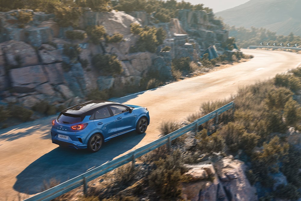 Una Puma Gen-E blu percorre una tortuosa strada di montagna.