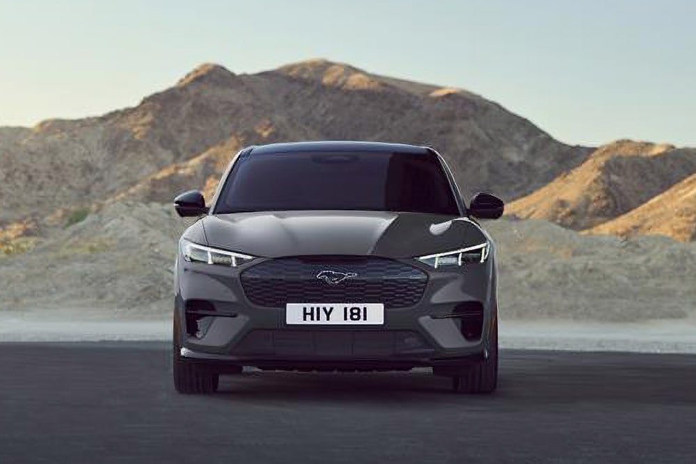 Vista frontale di una Ford Mustang Mach-E nera, parcheggiata davanti a un paesaggio montuoso.