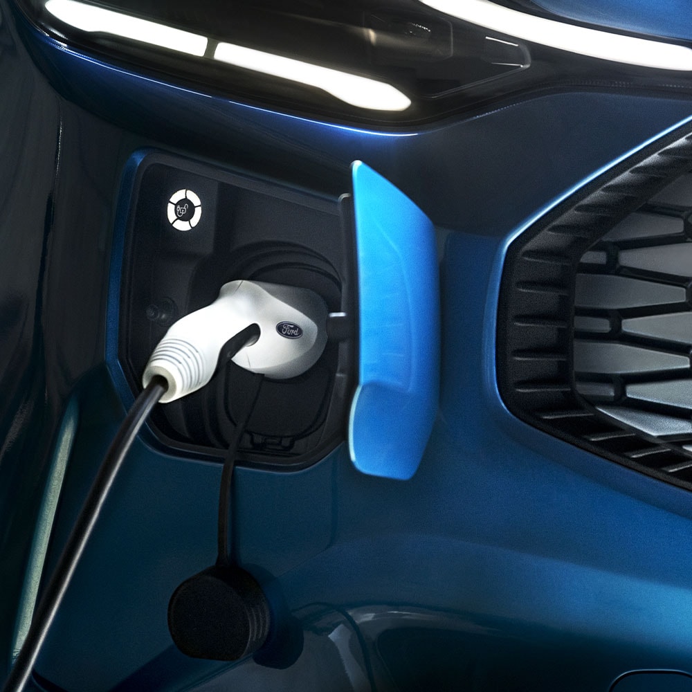 Una stazione di ricarica per auto elettriche con un caricabatterie collegato per veicoli elettrici davanti a un veicolo Ford blu.