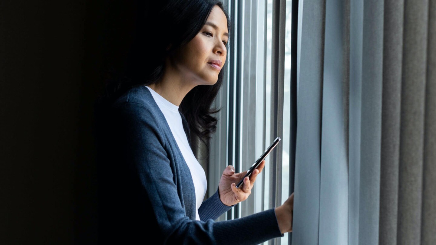 Una donna tiene in mano uno smartphone e guarda fuori dalla finestra
