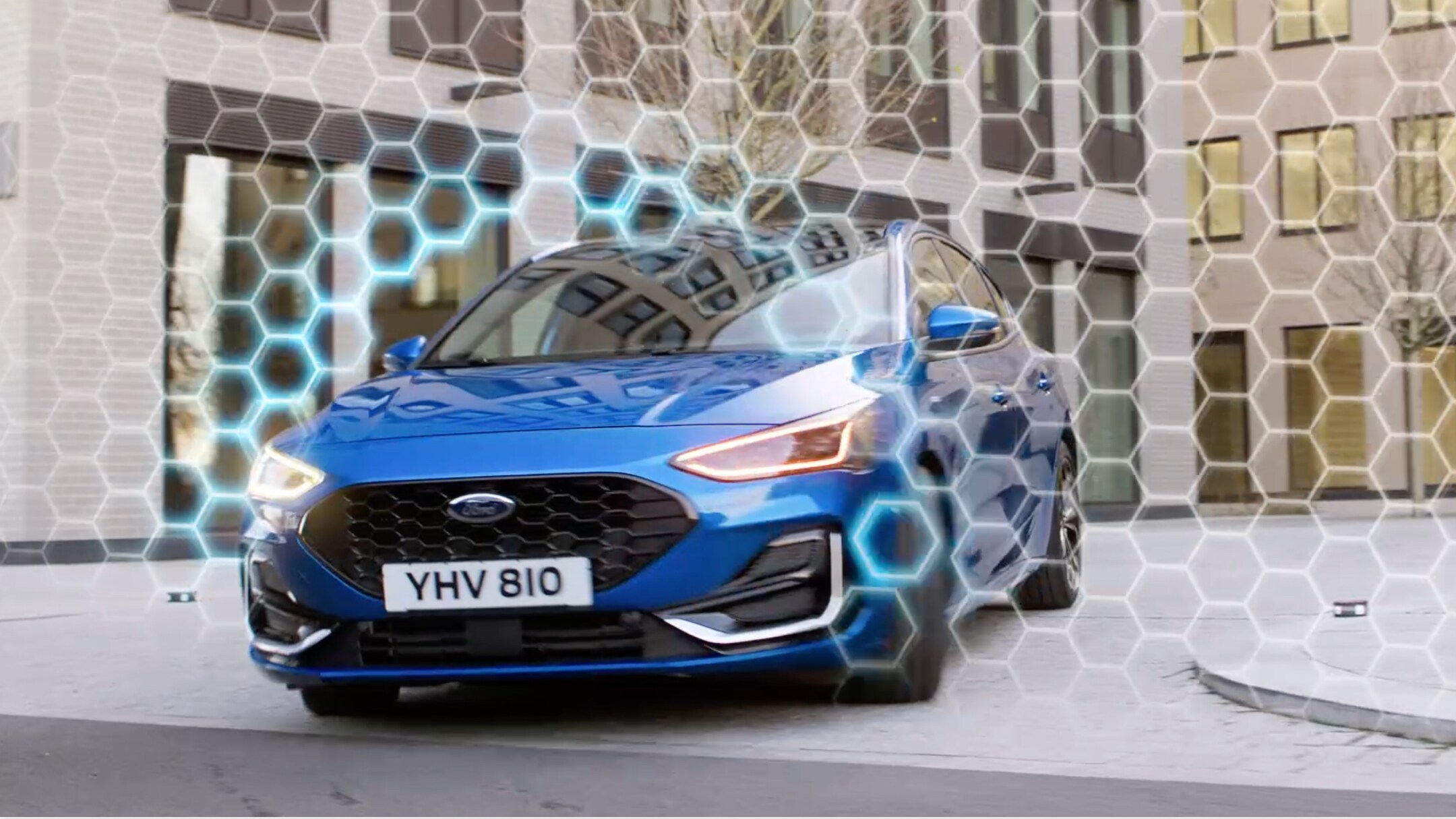 Ford Focus blu, vista frontale a tre quarti, in transito in curva sfonda un’animazione grafica di protezione