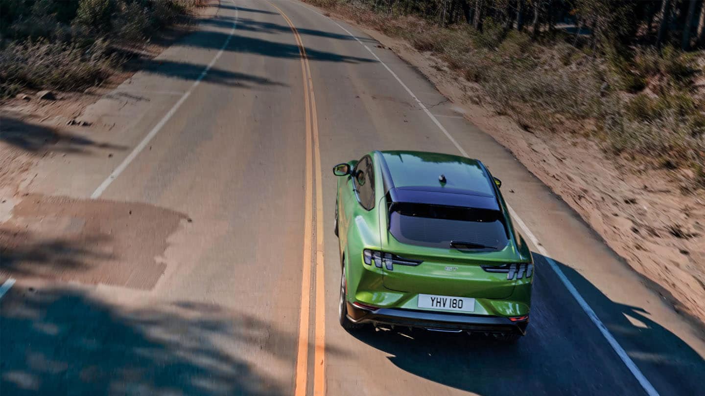 Una Ford Mustang Mach-E GT verde in marcia su una strada di montagna delimitata da alberi.
