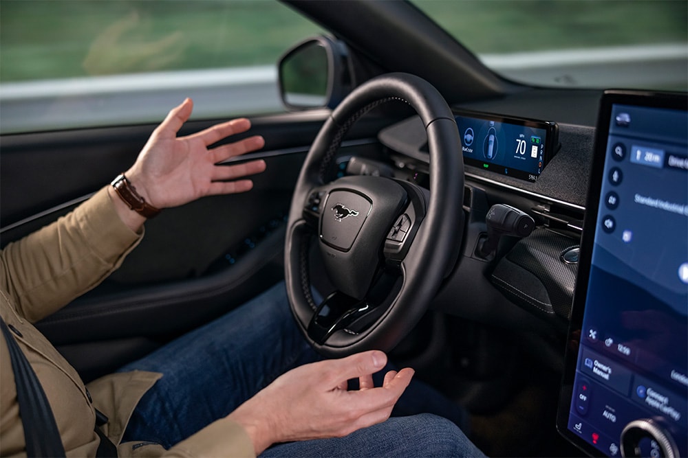 Le mani del conducente sospese sopra il volante della Mustang Mach-E a dimostrazione della tecnologia BlueCruise che consente la guida autonoma.