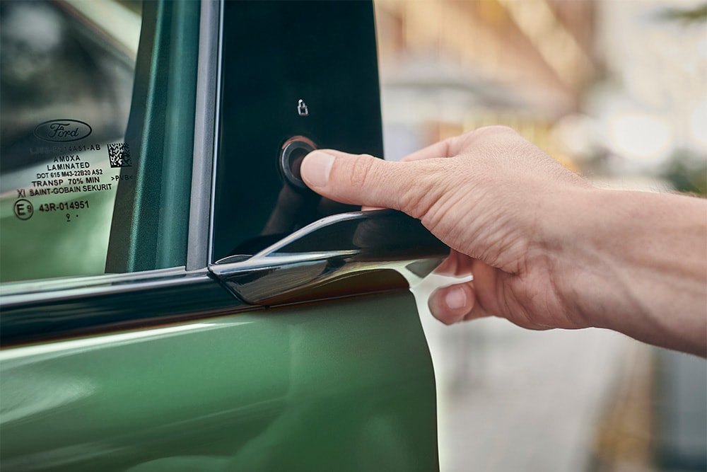 Mano che preme su un pulsante della portiera aprendo così una Ford Mustang Mach-E verde.