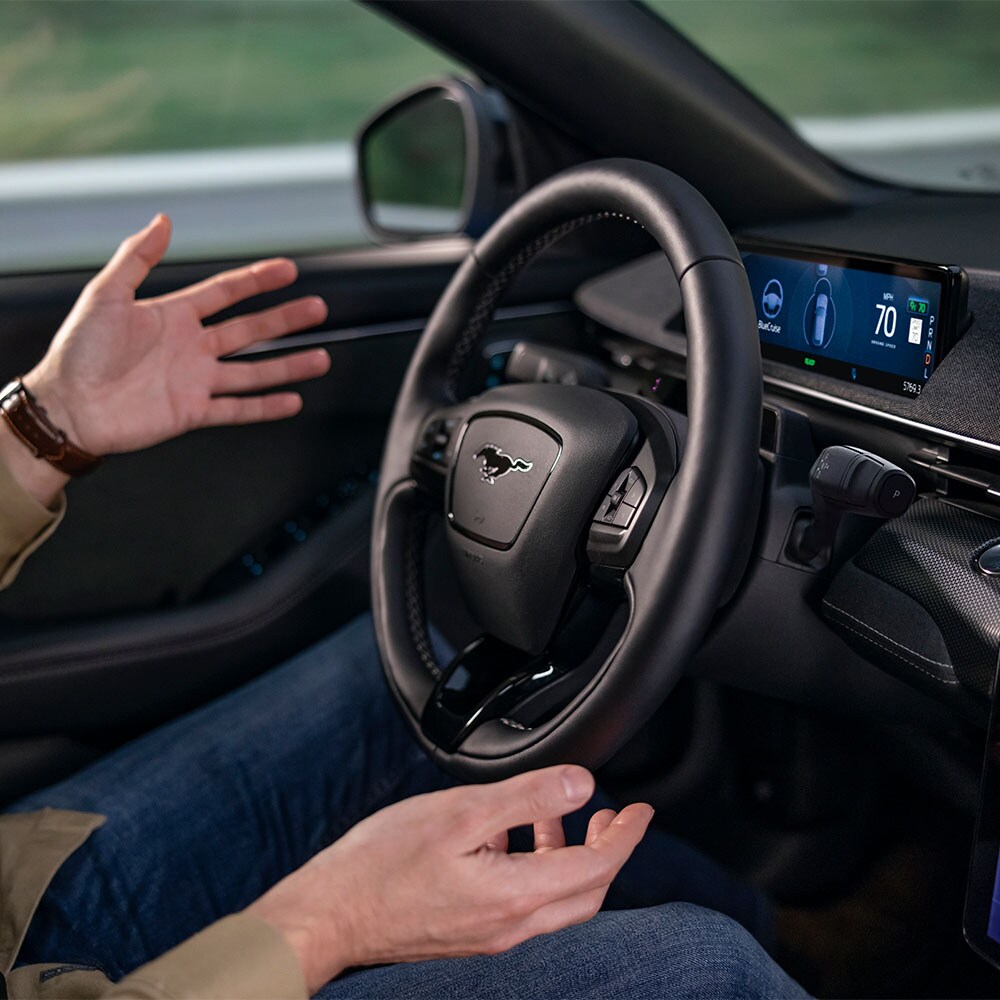 Le mani del conducente sospese sopra il volante della Mustang Mach-E a dimostrazione della tecnologia BlueCruise che consente la guida autonoma.