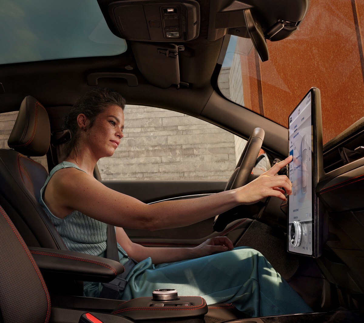 Ford Mustang Mach- E. Vista degli interni. La conducente utilizza il touchscreen del Ford SYNC 4