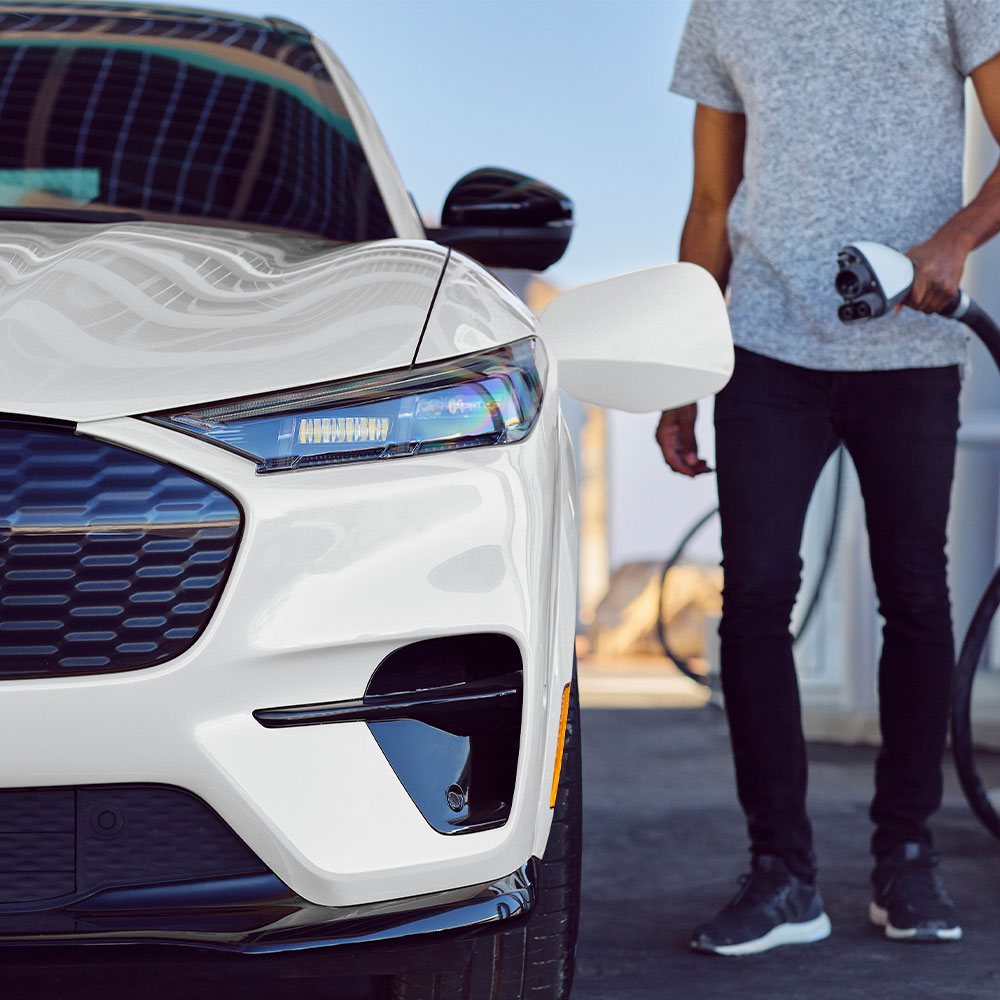 Persona che ricarica una Ford Mustang Mach-E bianca con un cavo per veicoli elettrici.