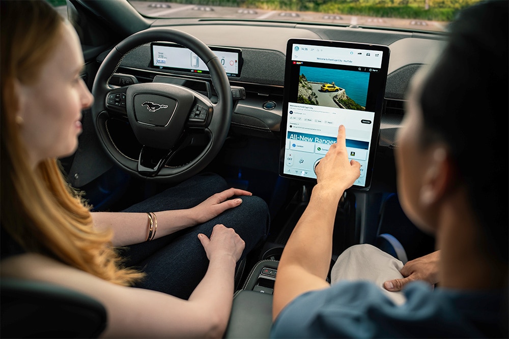 Vista ravvicinata della dashboard di un Mustang Mach-E, mentre un conducente indica il touchscreen.