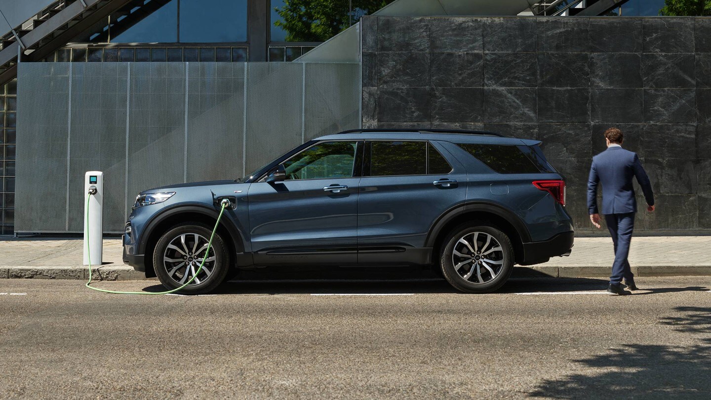 Ford Explorer Plug-In Hybrid blu. Vista laterale. In fase di ricarica presso una stazione pubblica.