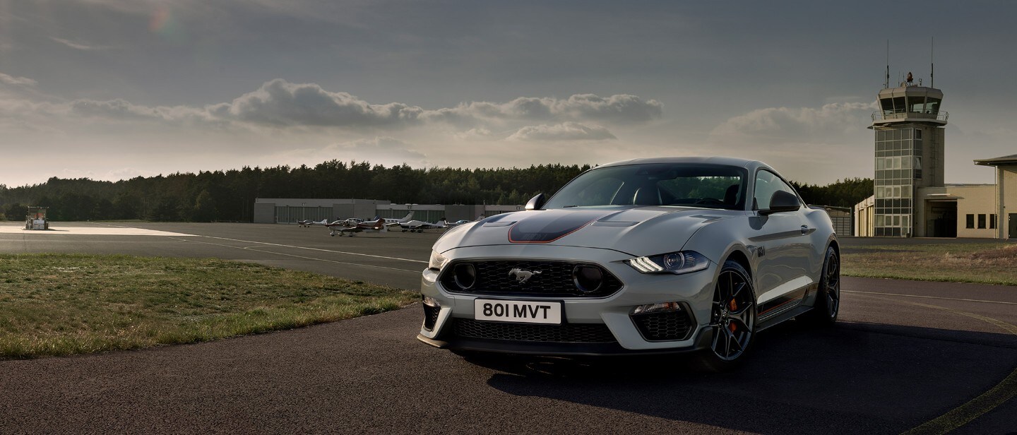 Ford Mustang Mach 1 bianca. Vista frontale a tre quarti, in marcia su un circuito all’ora del tramonto