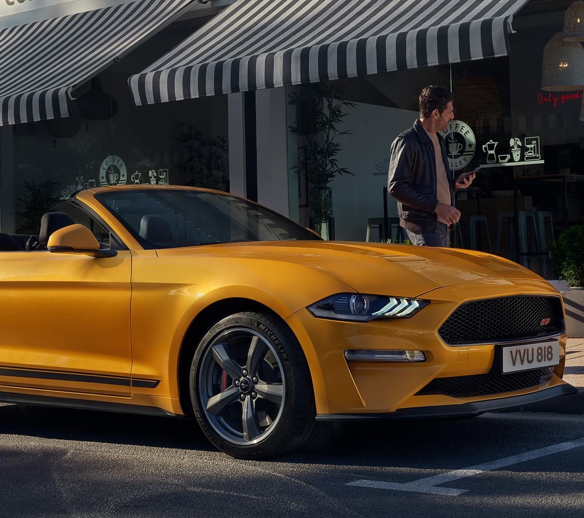 Ford Mustang California arancione. Vista frontale a tre quarti, parcheggiata davanti a un negozio