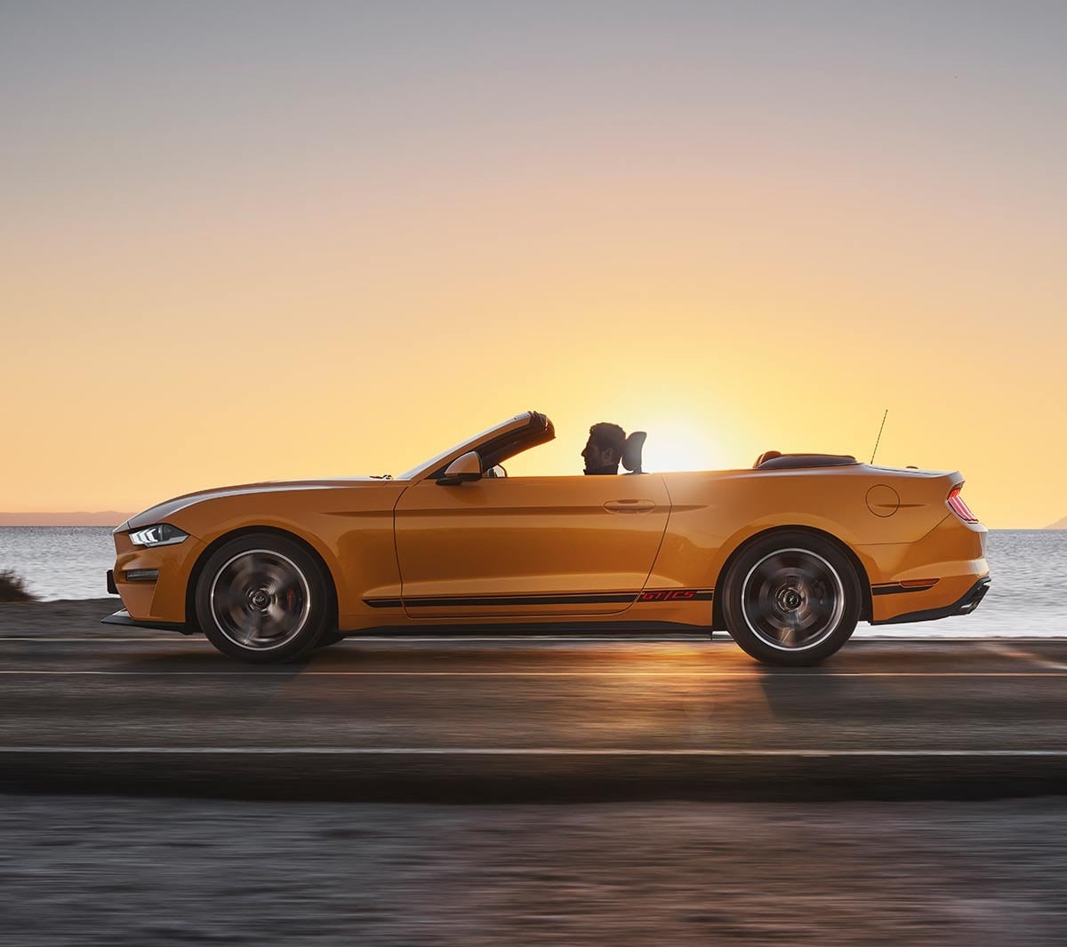 Ford Mustang California arancione. Vista laterale, in marcia nella natura al tramonto.