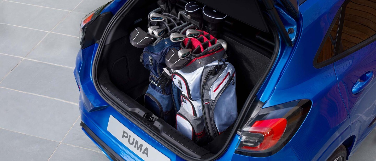 Ford Puma ST grigia, vista posteriore a tre quarti dall’alto, con una donna che inserisce un tappetino da yoga nel bagagliaio aperto