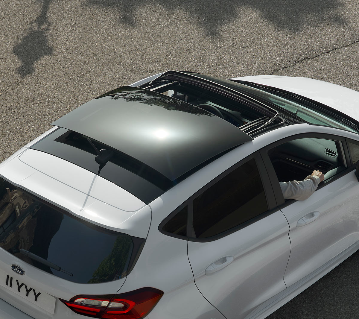 Ford Fiesta bianca. Vista posteriore a tre quarti dall’alto del modello con tetto panoramico apribile, in transito su una strada.