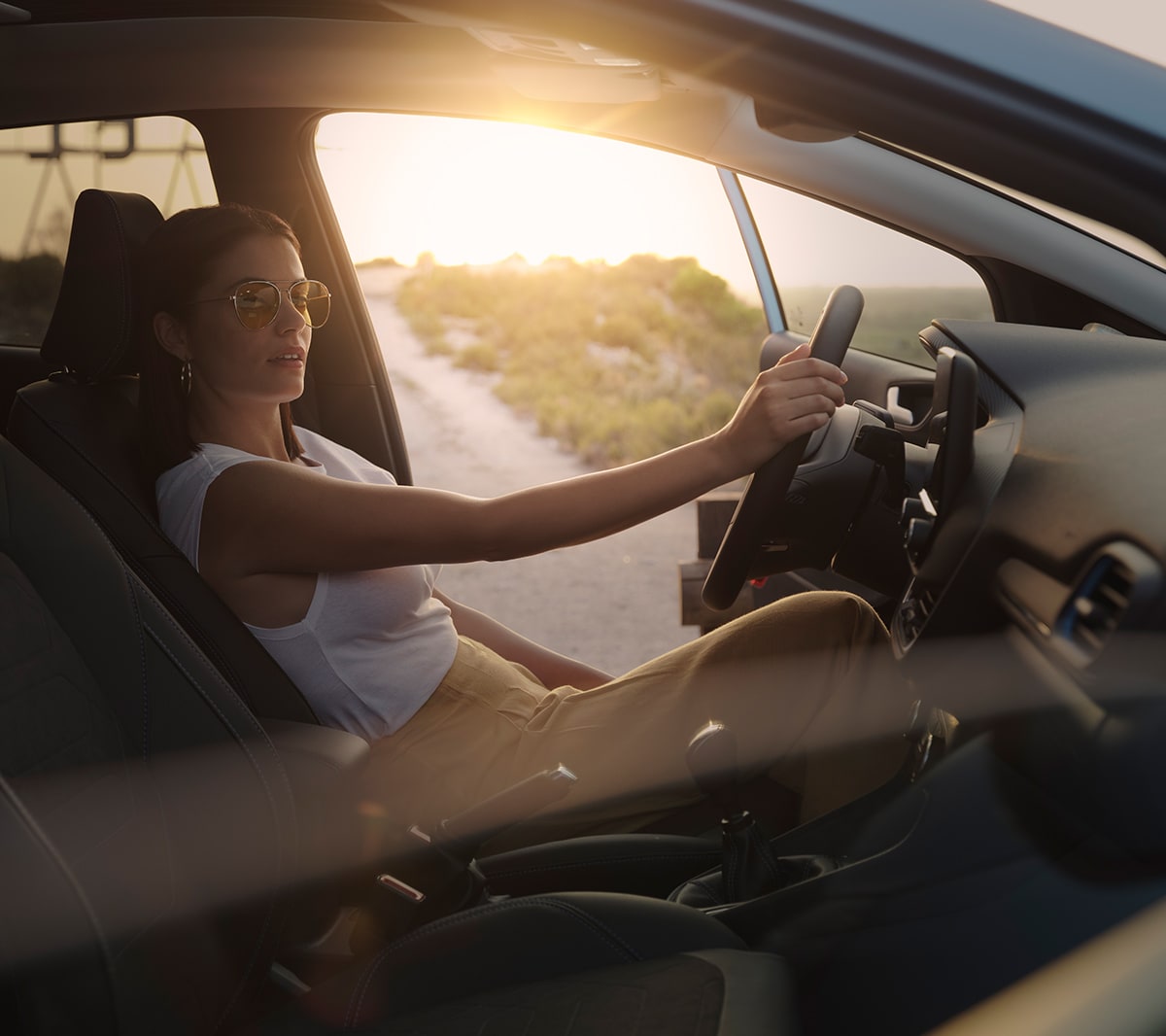 Ford Fiesta. Vista degli interni. Una donna è seduta sul sedile del conducente con la portiera aperta. Sullo sfondo un tramonto.