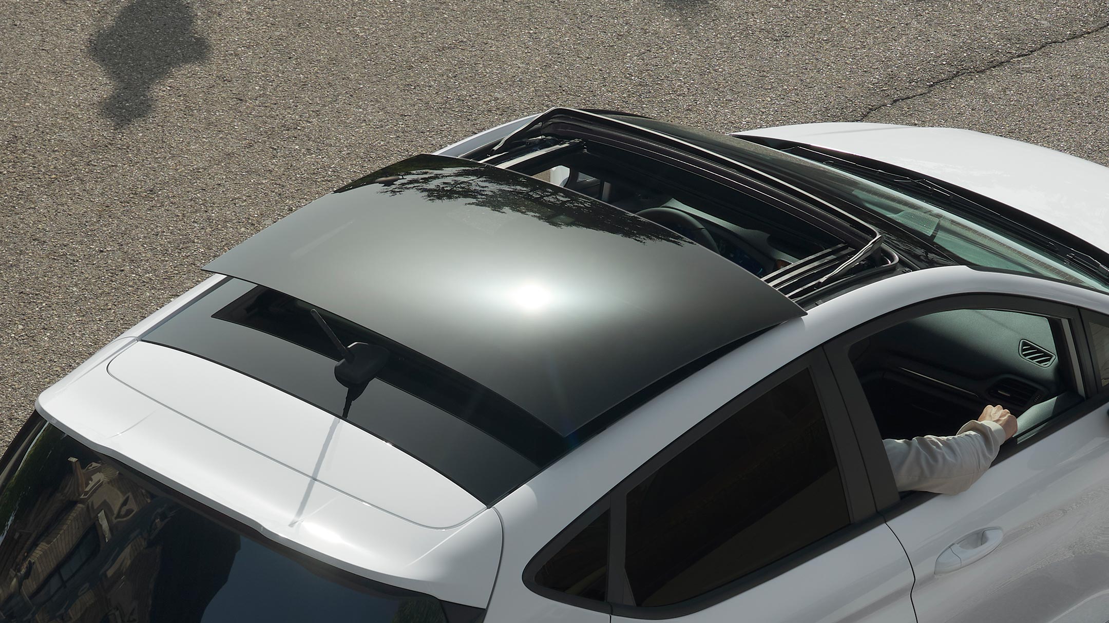 Ford Fiesta bianca. Vista posteriore a tre quarti dall’alto del modello con tetto panoramico apribile, in transito su una strada.