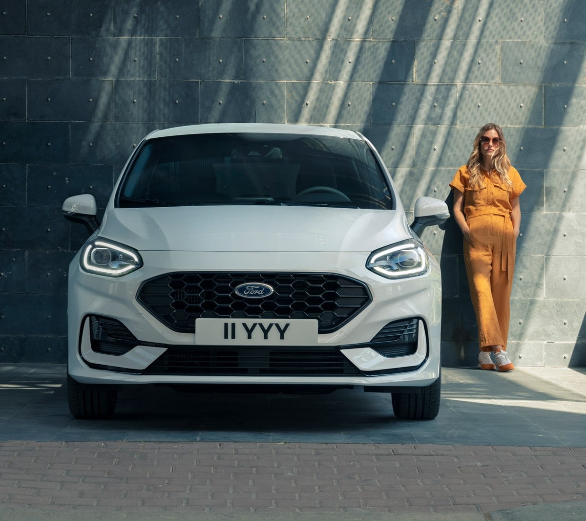Ford Fiesta bianca. Vista frontale, in fase di parcheggio davanti a un edificio moderno con accanto una donna.