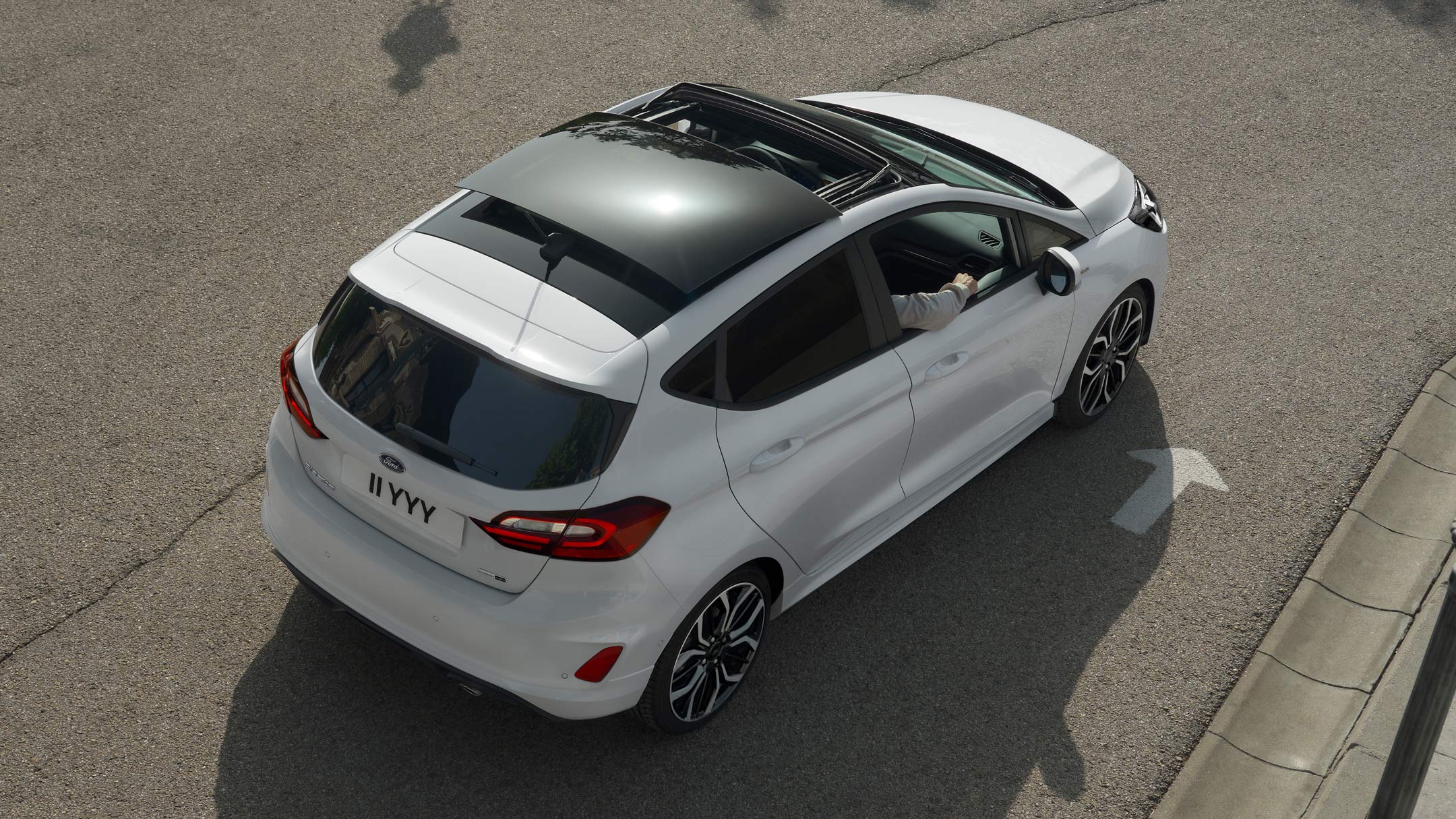 Ford Fiesta bianca. Vista posteriore a tre quarti dall’alto con visuale sul tetto panoramico apribile, in marcia su una strada.