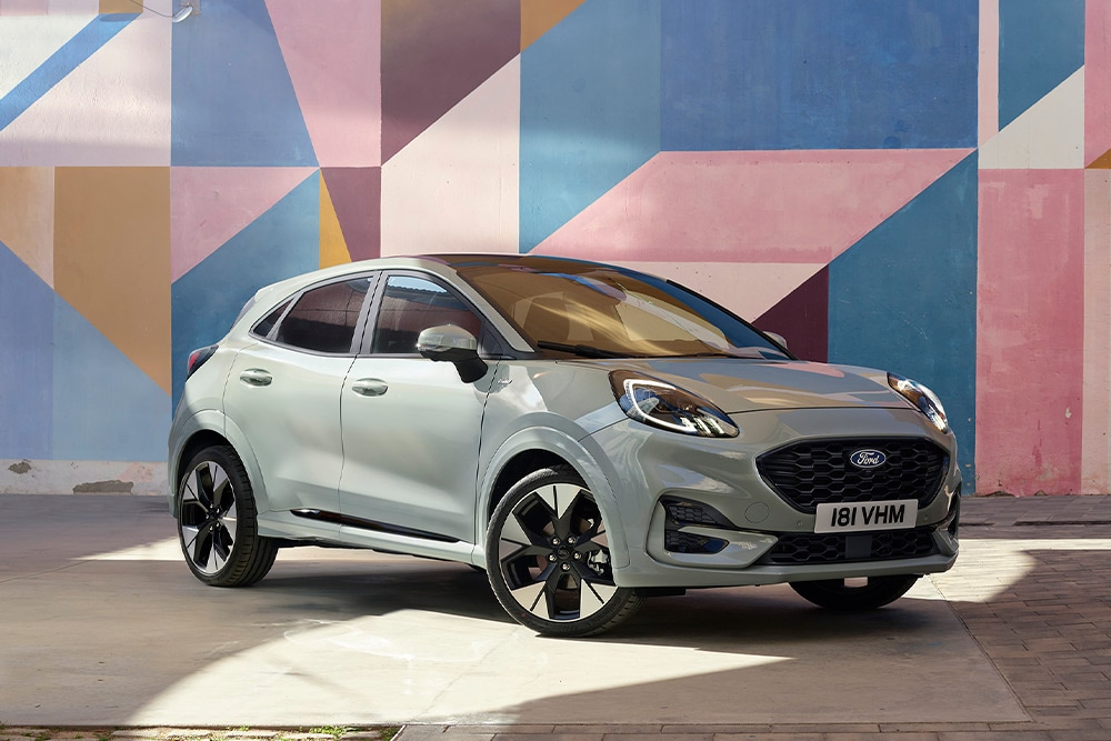 Una Ford Puma SUV argento parcheggia davanti a un muro decorato con forme geometriche colorate.