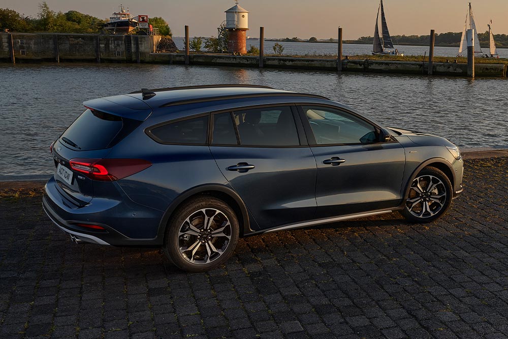 Una Ford Focus Active Turnier blu scura parcheggiata presso uno specchio d’acqua al crepuscolo.