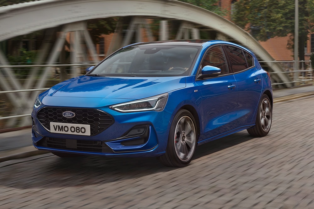 Una Ford Focus modello hatchback blu è in marcia su un ponte.