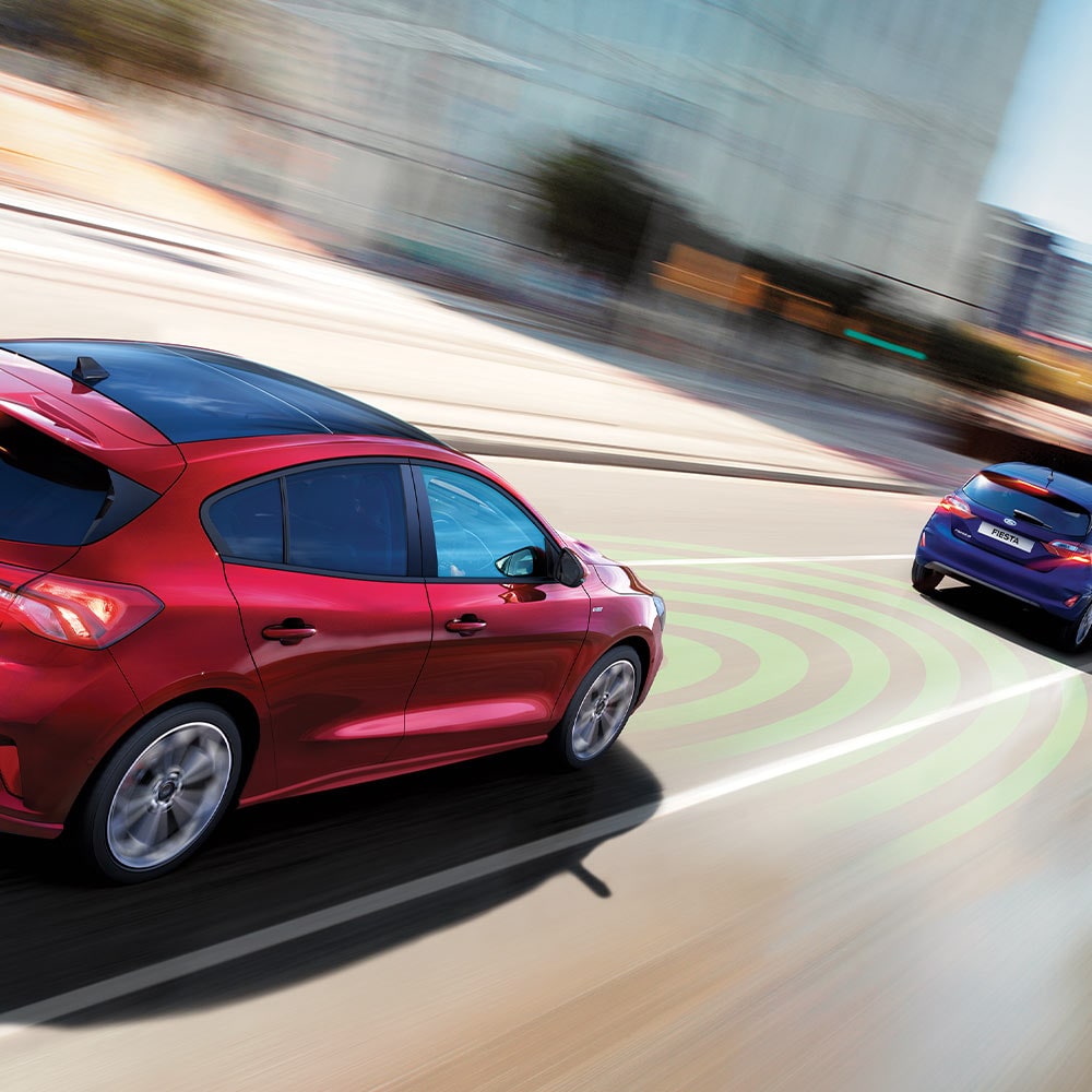 Immagine grafica che mostra una Ford Focus rossa i cui sensori (rappresentati da linee blu) riconoscono il veicolo che sta davanti al fine di attivare una frenata d’emergenza.