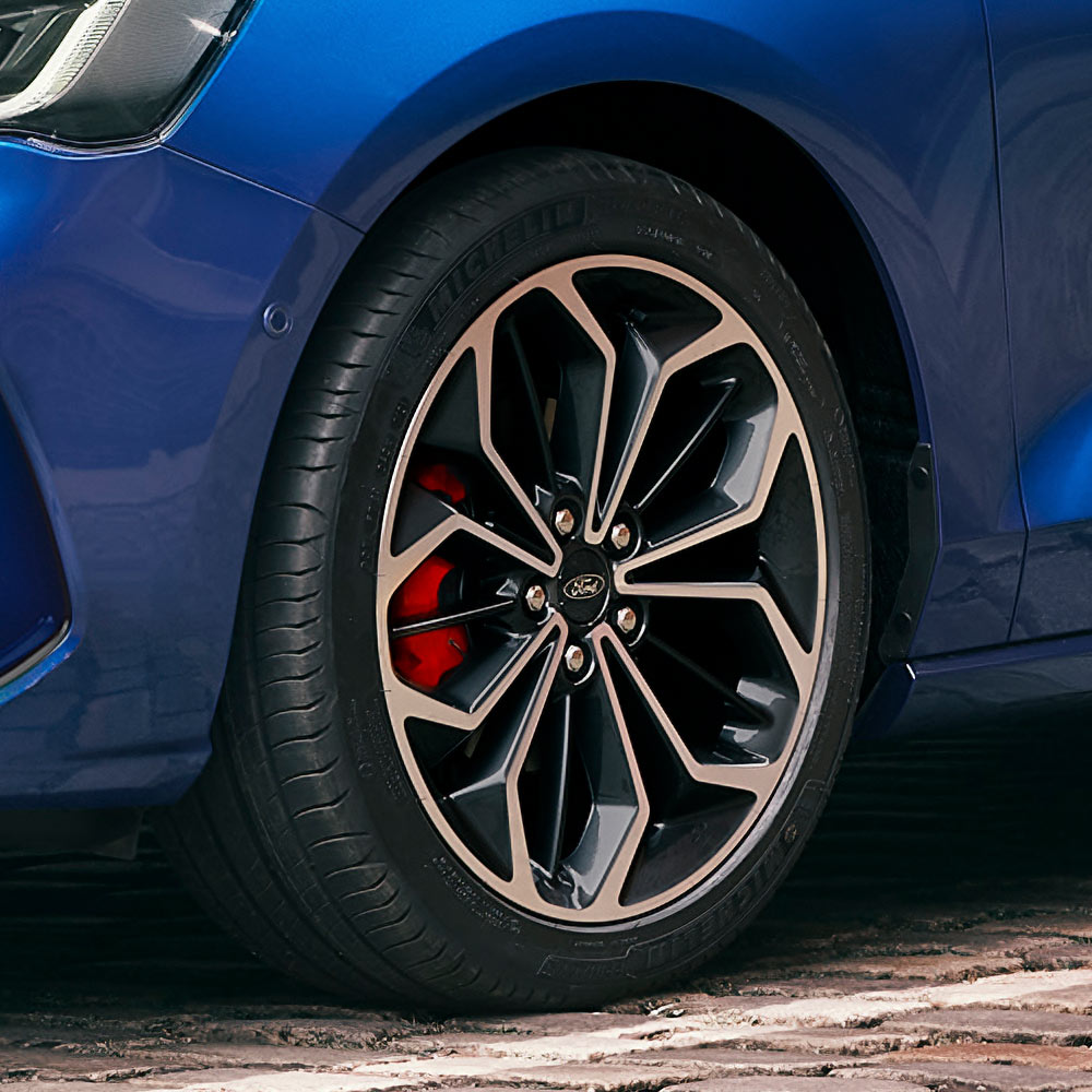 Vista ravvicinata dei cerchi in lega grigi con pinze frenanti rosse di una Ford Focus blu.