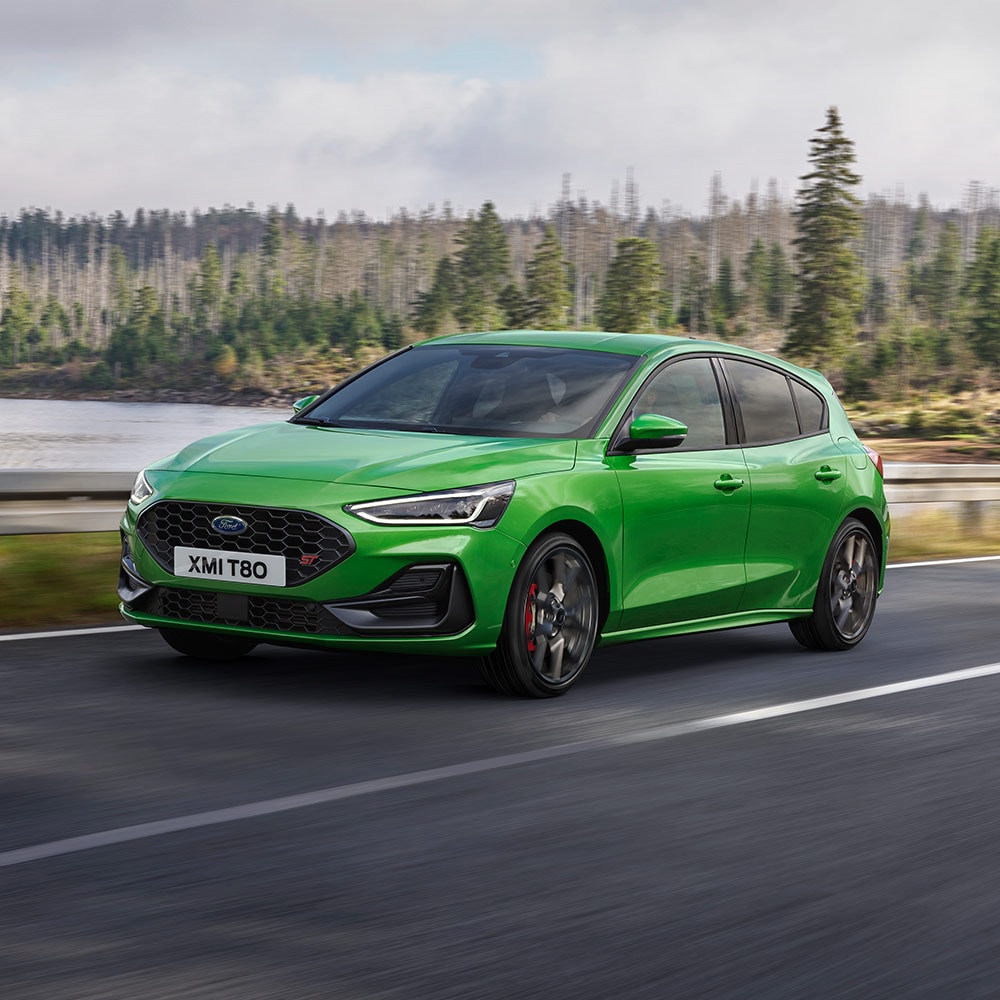 Una Ford Focus ST color Mean Green in marcia su una strada piena di curve fiancheggiata da alberi.