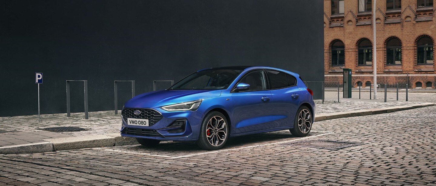 Ford Focus ST-Line blu. Vista frontale a tre quarti, parcheggiata in un’area industriale.