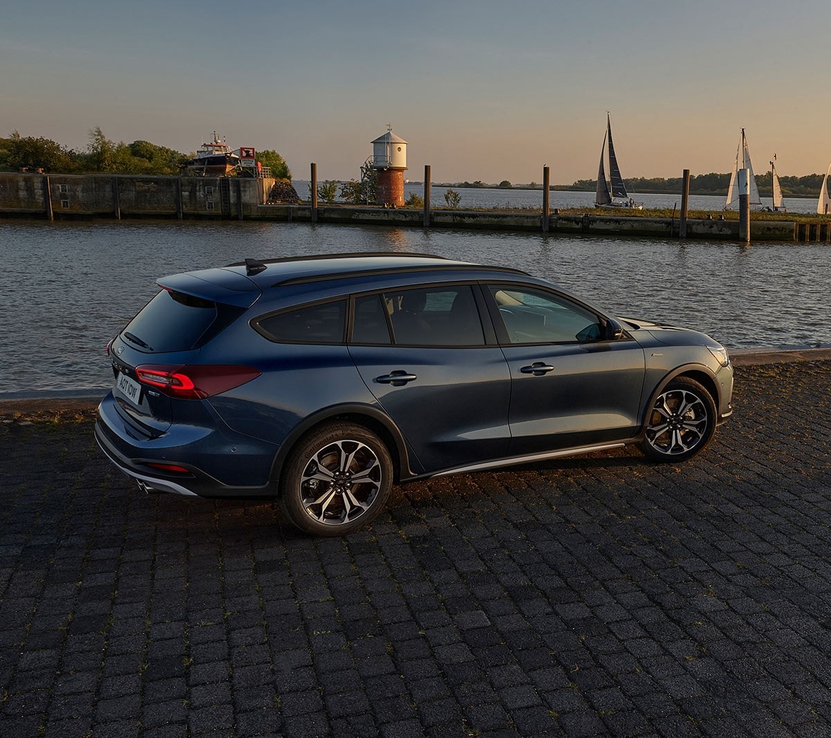 Ford Focus blu. Vista posteriore a tre quarti, parcheggiata davanti a un lago al tramonto.